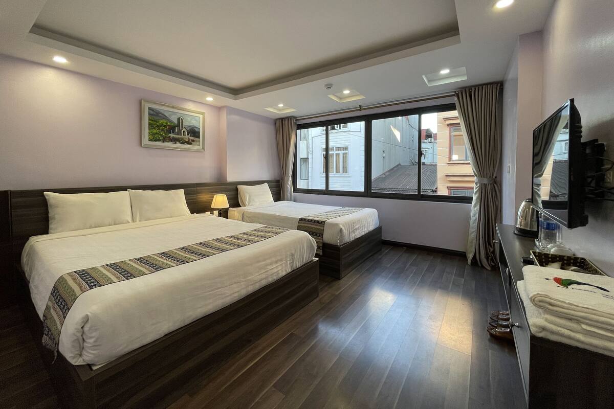 Habitación de hotel con dos camas, un ventanal grande, un televisor de pantalla plana y una mesita con un hervidor.