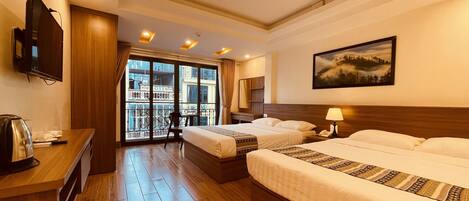 Quarto de hotel com duas camas, uma escrivaninha com chaleira, televisão e varanda com vista para a cidade.