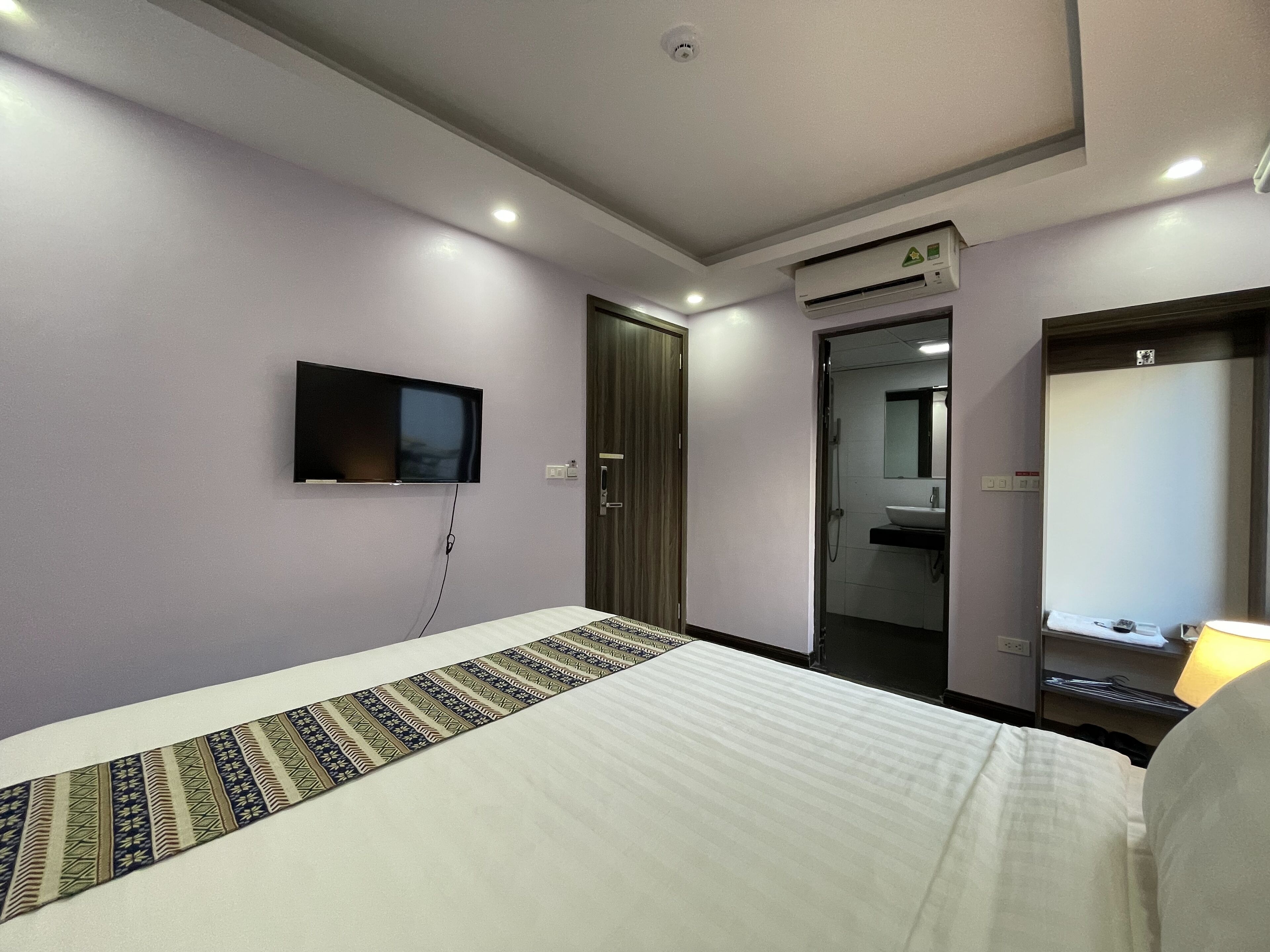 A hotel room with a bed, a television mounted on the wall, a bathroom with a mirror and sink, and a door leading to another room.