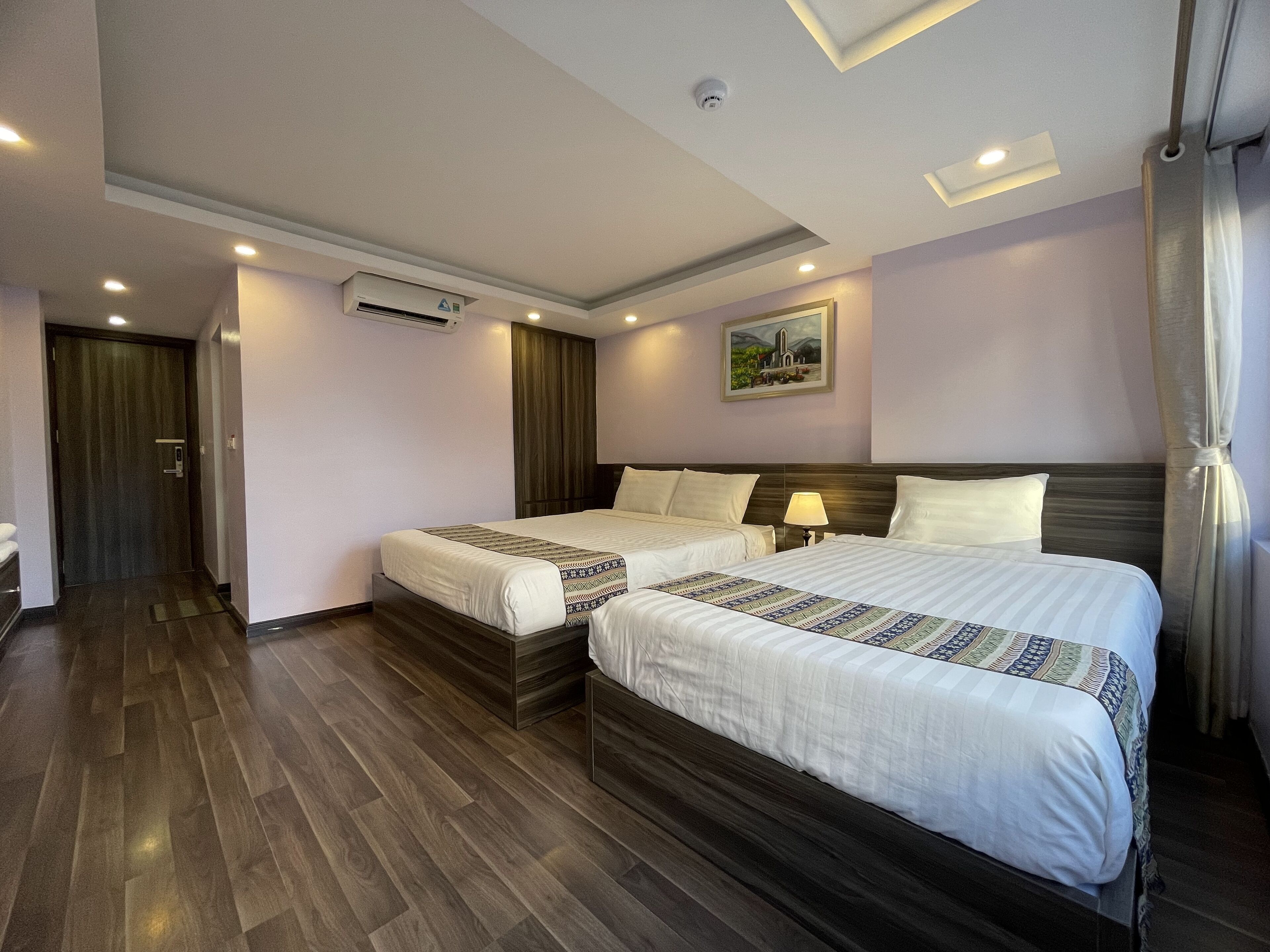 Habitación de hotel con dos camas, suelo de madera, un cuadro en la pared e iluminación empotrada en el techo.