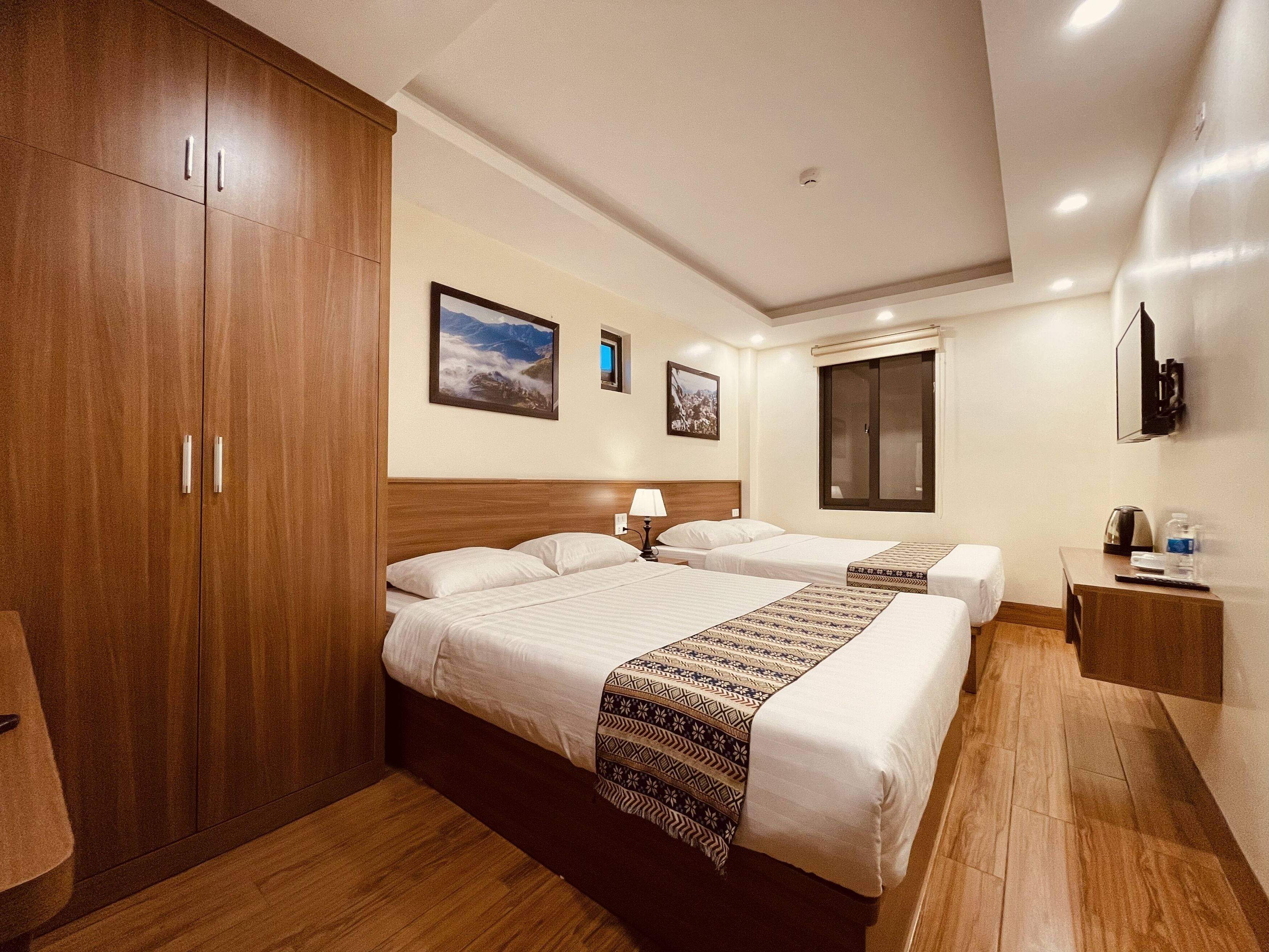A hotel room with two beds, wooden wardrobe, a TV, and a window with a view.