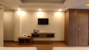 A hotel room with two beds, a wooden cabinet, a TV mounted on the wall, and a small table with a kettle and cups.