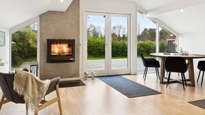 A modern living room with a fireplace, a dining area with a table and chairs, and large sliding glass doors leading to a garden. - "Frithlef" - 1.3km from the sea by Interhome (Græsted)