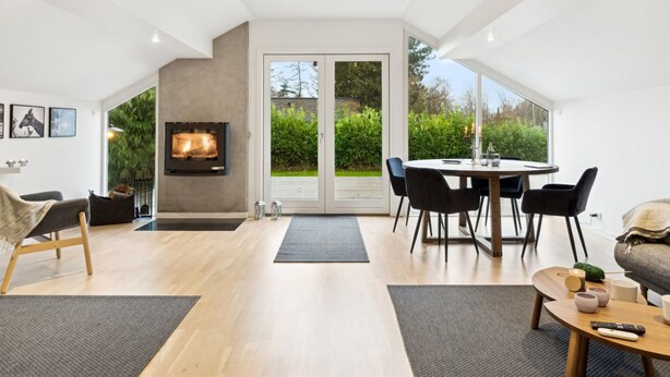 A modern living room with a fireplace, a dining area, and large windows offering a view of the garden. - "Frithlef" - 1.3km from the sea by Interhome (Græsted)