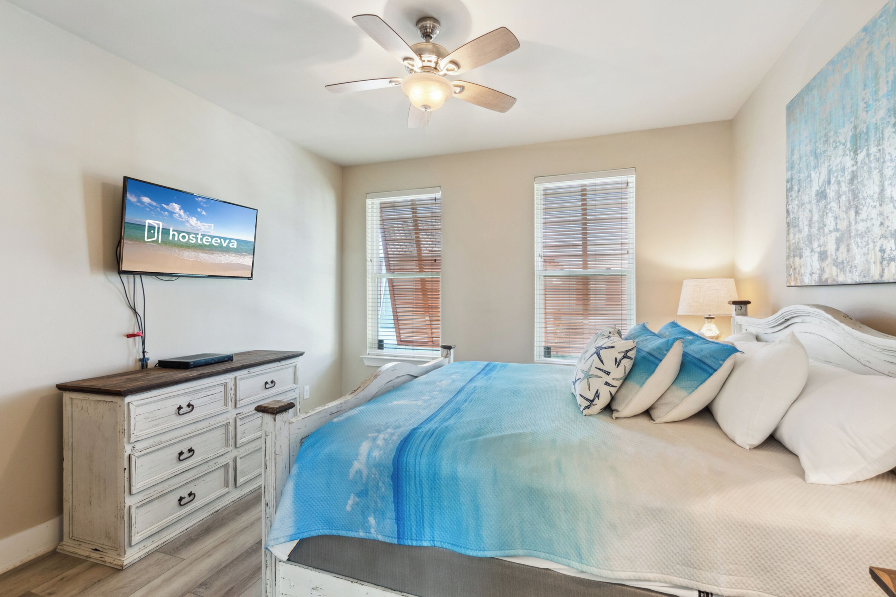 A bedroom with a bed, a ceiling fan, a TV on the wall, and a window with blinds.
