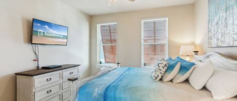 A bedroom with a bed, a ceiling fan, a TV on the wall, and a window with blinds.