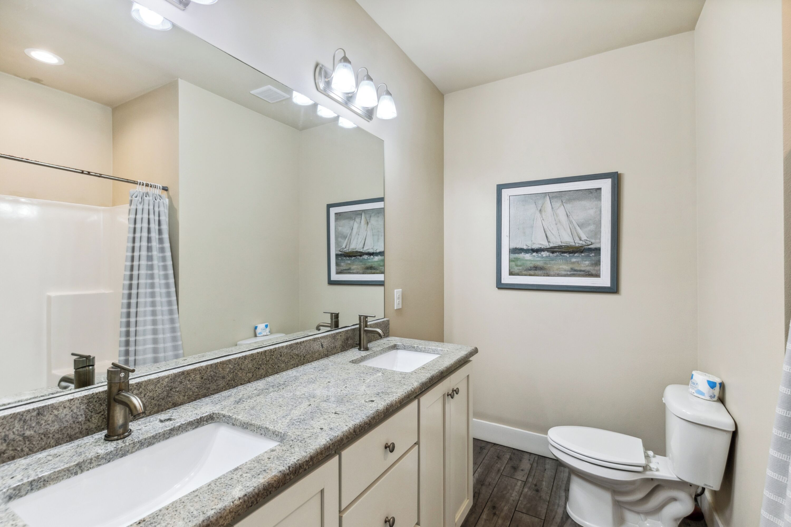 A bathroom with two sinks, a toilet, a shower curtain, and a large mirror.
