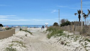 Un sentier de sable qui longe la plage et mène à l’océan, avec des parasols et des chaises de plage.