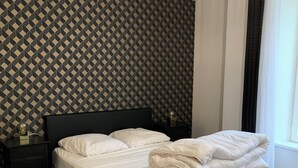 Una cama bien hecha con ropa blanca, cabecera negra y un papel tapiz estampado al fondo.