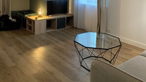 Una sala moderna con un televisor de pantalla plana, una mesa de centro de vidrio y una lámpara colgante.