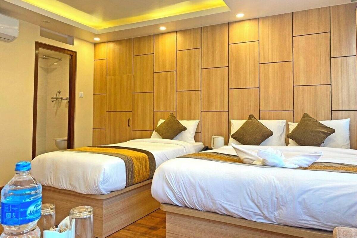 A hotel room with two beds, wooden paneling on the walls, a shower area, and a water bottle on the floor.