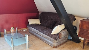 A living room with a glass coffee table, a brown sofa with cushions, a wooden cabinet, and a red wall.
