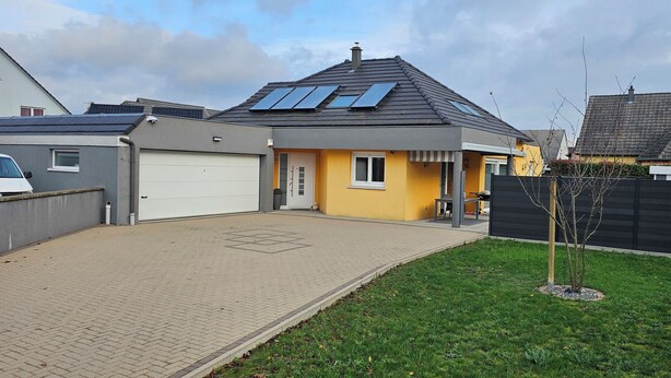 A residential house with a garage, solar panels on the roof, and a small garden area.