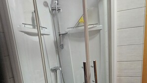 A corner shower with a glass door, a vanity with drawers, and a tiled floor.