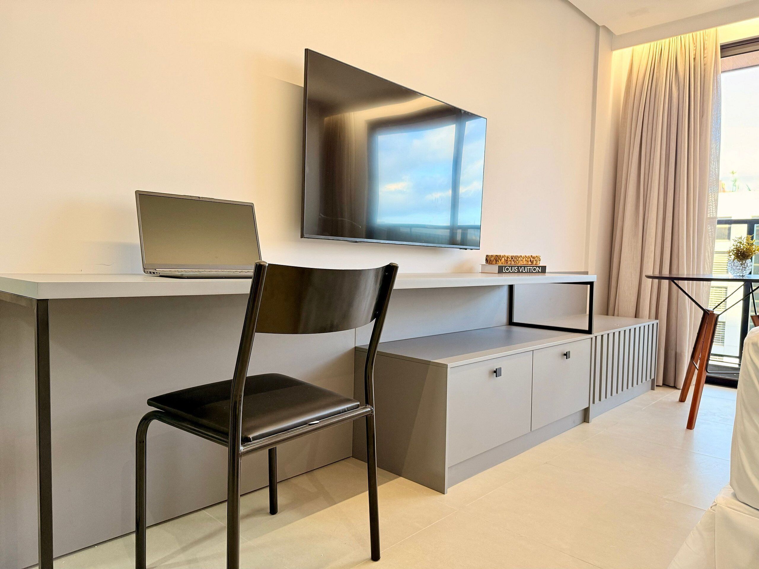 A modern hotel room with a desk, chair, television, and a view of the outdoors.