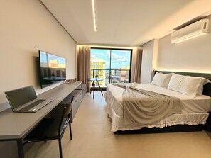 A hotel room with a bed, a desk with a laptop, a TV, and a view of the city through large windows. - Way Tambaú  (João Pessoa)