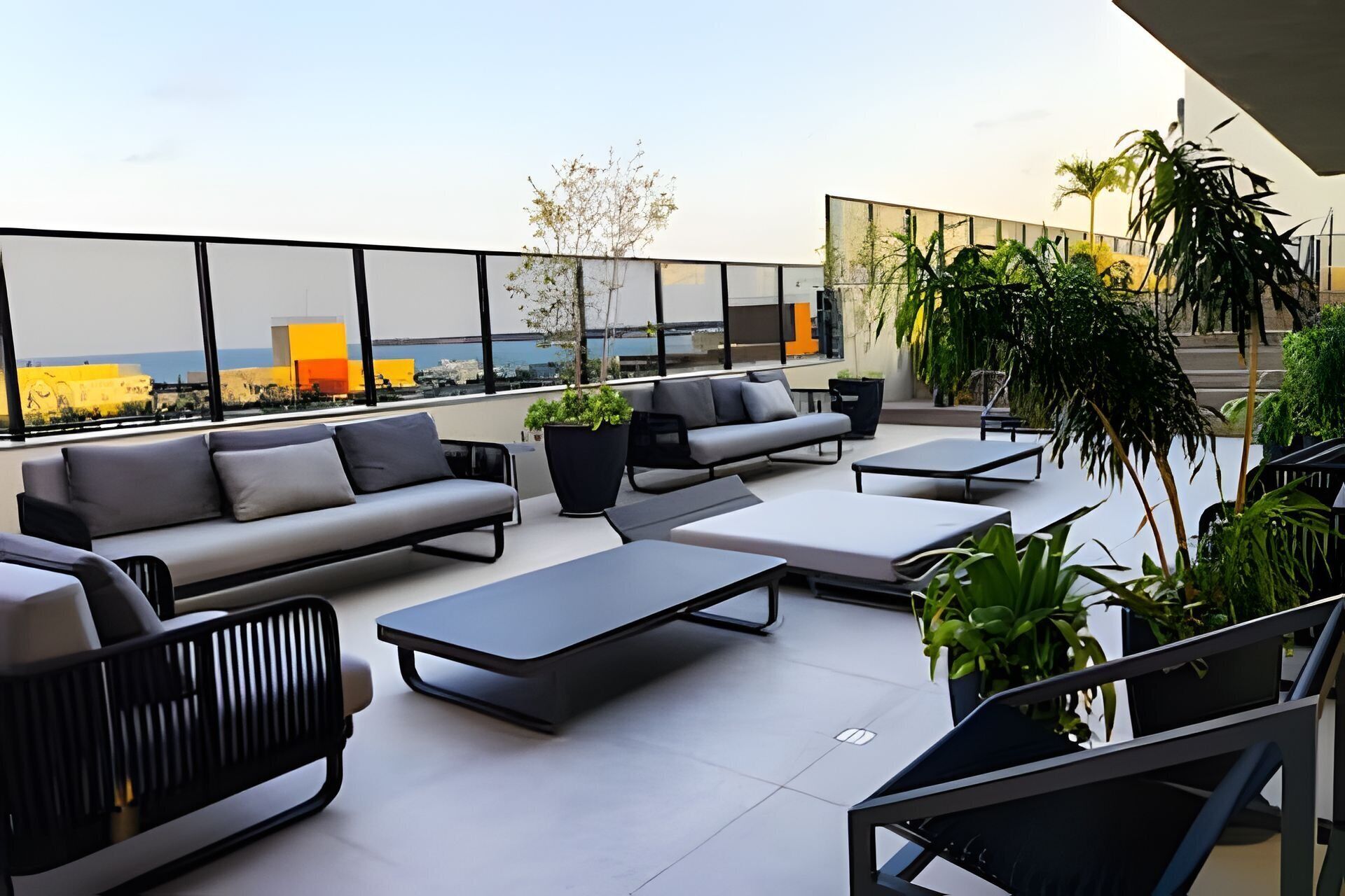 A rooftop terrace with modern outdoor furniture, including sofas and tables, surrounded by potted plants.