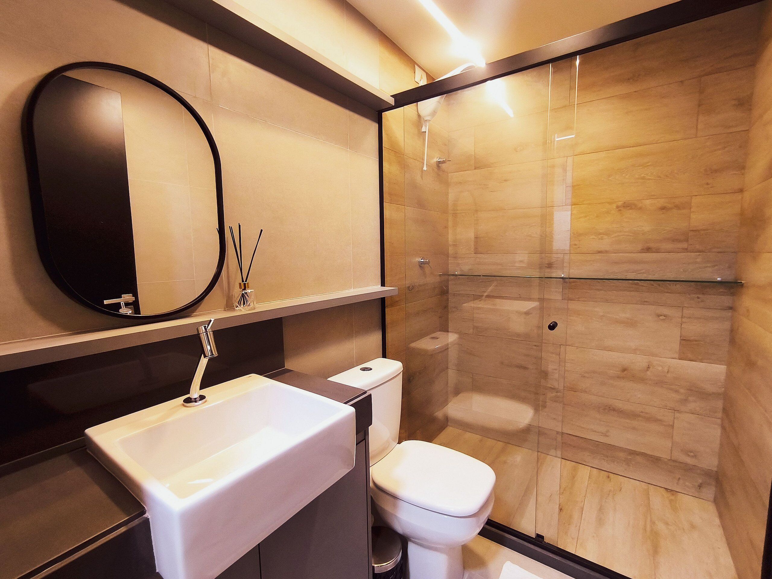 Une salle de bain moderne avec un grand miroir, un lavabo blanc, des toilettes et une douche à parois de verre.