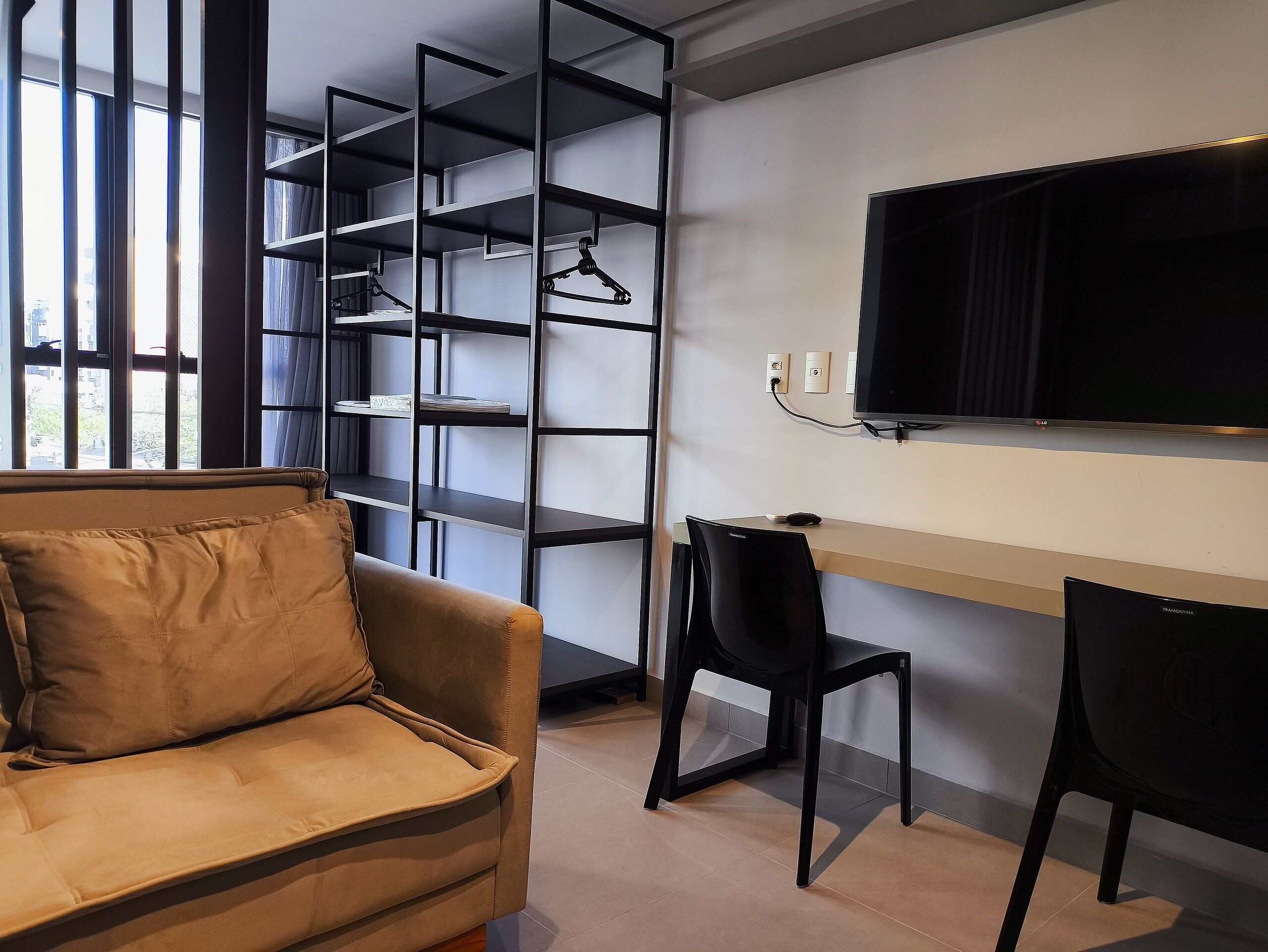 A modern room with a sofa, a desk with a chair, a TV, and a shelving unit.