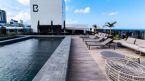 A rooftop pool area with lounge chairs and a modern building with a large 'E' logo. - Way Tambaú  (João Pessoa)