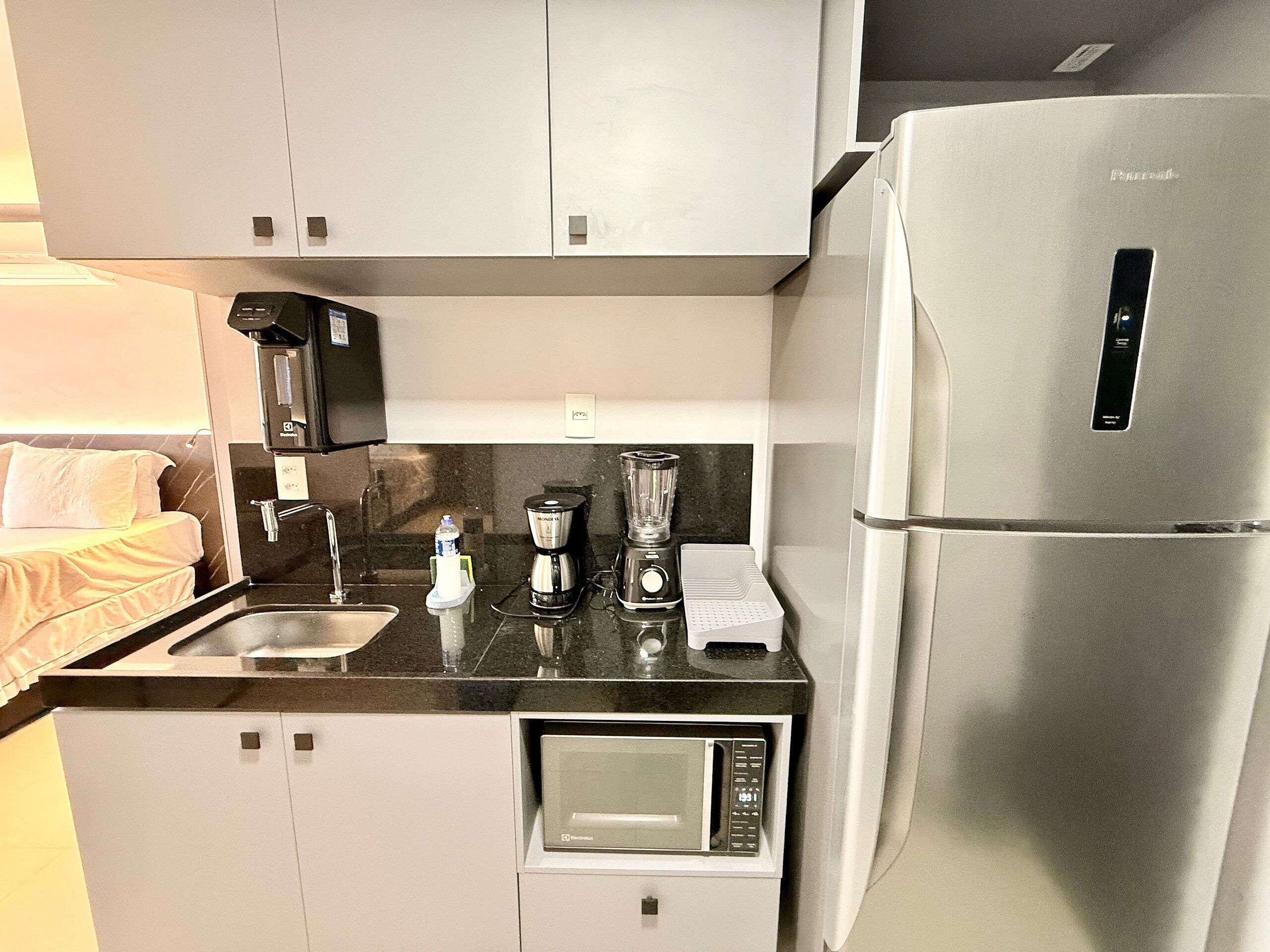 A compact kitchenette with a refrigerator, microwave, blender, coffee maker, and a small sink.