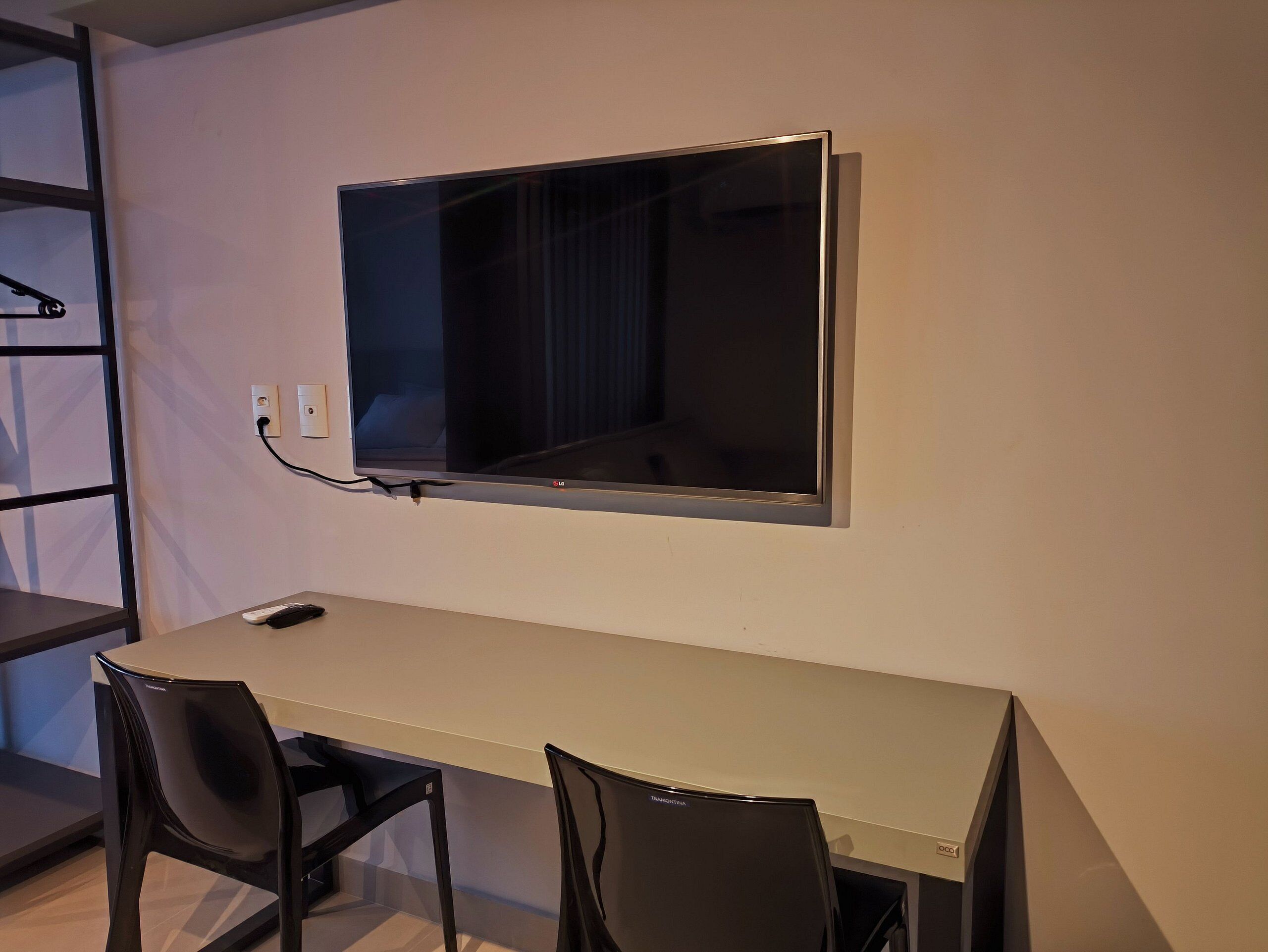 Una habitación moderna con una televisión de pantalla plana montada en la pared, una pequeña mesa con dos sillas y una estantería a la izquierda.