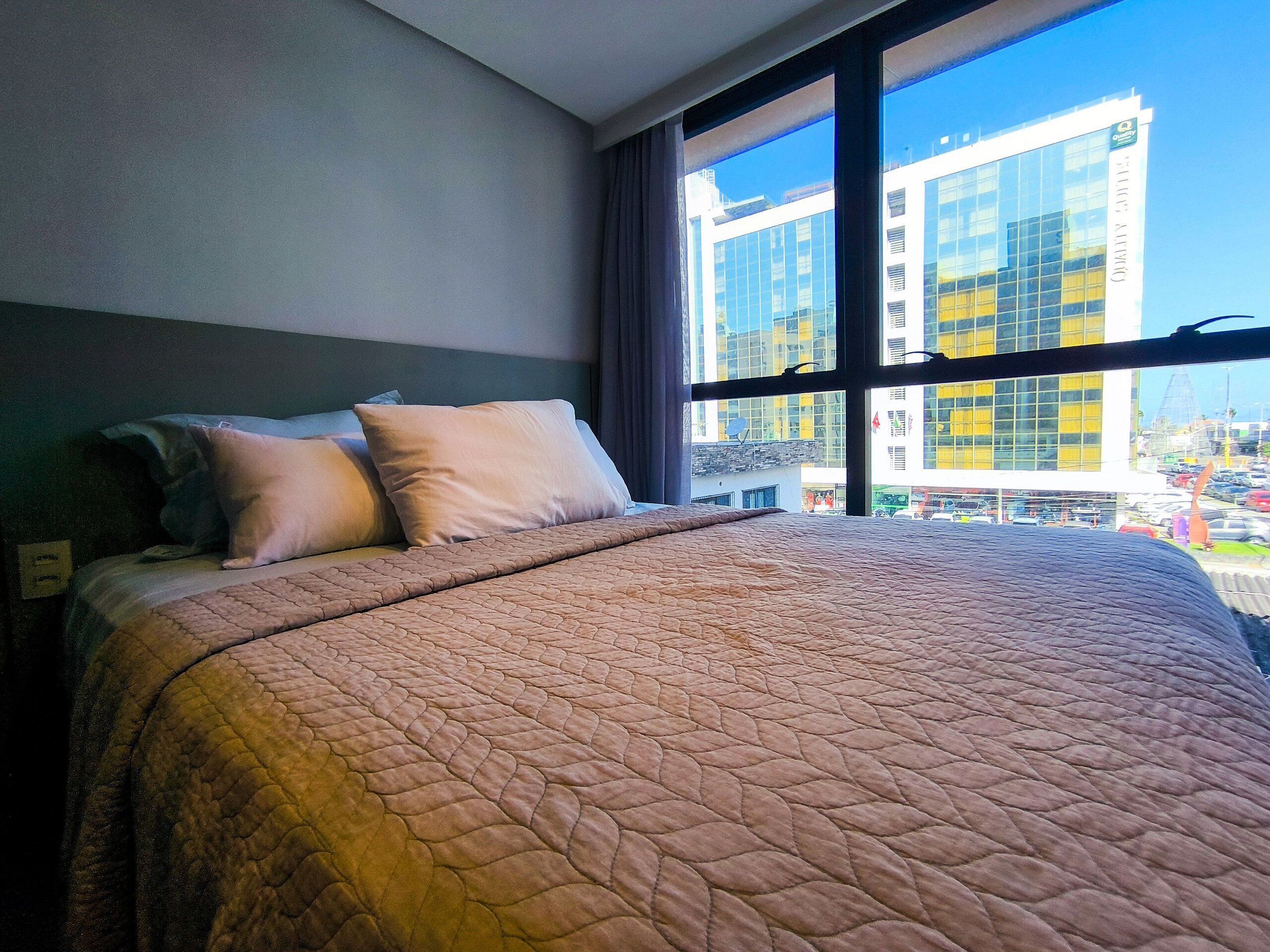 A hotel room with a large bed, a view of a modern building, and a window with curtains.