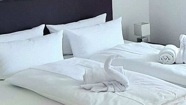 A neatly made bed with white linens and a folded towel on the side.