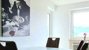 A modern dining area with a glass table, dark upholstered chairs, and a ceiling light fixture.