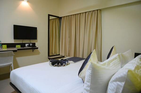A hotel room with a bed, a desk with a flat-screen TV, a chair, and a mirror. - Rajkiyam - A Business Hotel (Bengaluru)