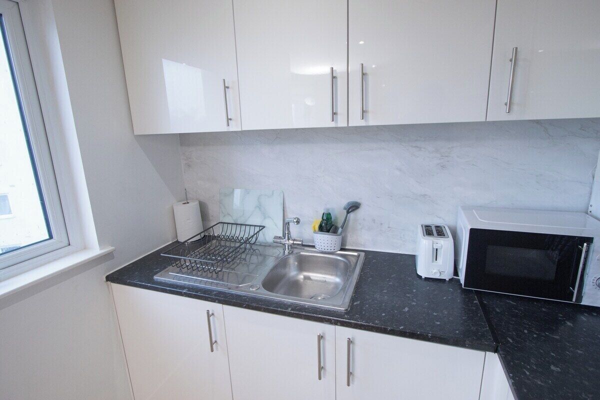 A kitchen with white cabinets, a black countertop, a stainless steel sink, a toaster, and a microwave.