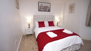 A bedroom with a white bed, red pillows, and a red blanket. There are two bedside tables with lamps. - 1-min walk to Town & Station I Near Airport I Parking (Luton)