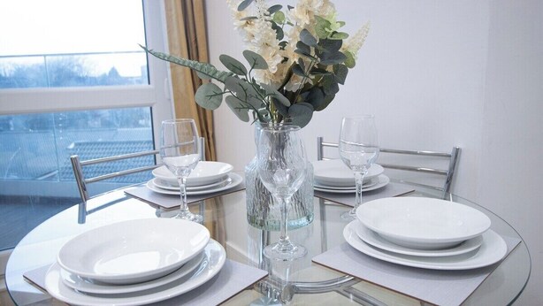 A dining table set with white plates, glasses, and a vase with flowers. - 1-min walk to Town & Station I Near Airport I Parking (Luton)