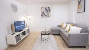 A modern living room with a grey sofa, a white entertainment unit, and a flat-screen TV displaying Netflix. - 1-min walk to Town & Station I Near Airport I Parking (Luton)