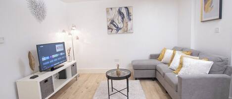 A modern living room with a grey sofa, a white entertainment unit, and a flat-screen TV displaying Netflix.