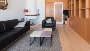 Een moderne woonkamer met een zwarte leren bank, een klein bijzettafeltje, een houten boekenkast en een open haard.