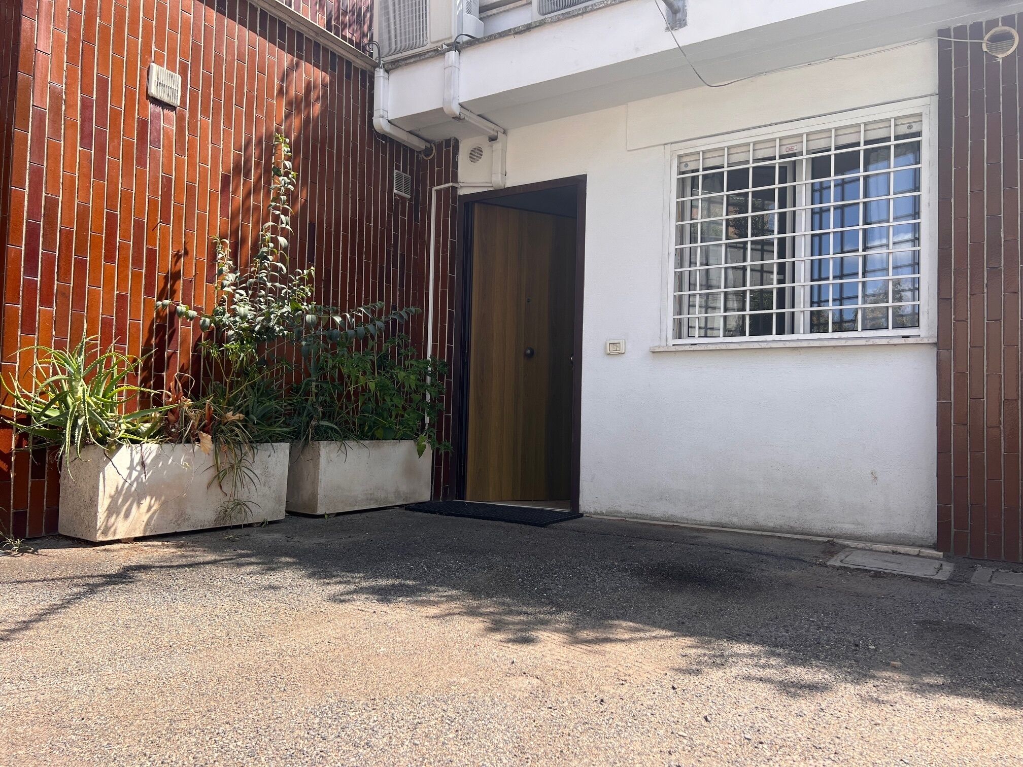 A small, enclosed courtyard with a gravel ground, a wooden fence, and potted plants.