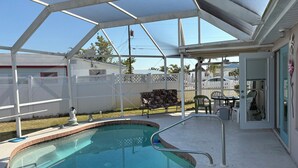 Une piscine extérieure couverte avec un toit en métal, un espace patio avec une table et des chaises, et une vue sur un quartier résidentiel.