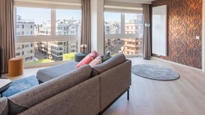 Ein modernes Wohnzimmer mit einem grauen Sofa, einem runden Couchtisch und Blick auf eine Skyline durch große Fenster.