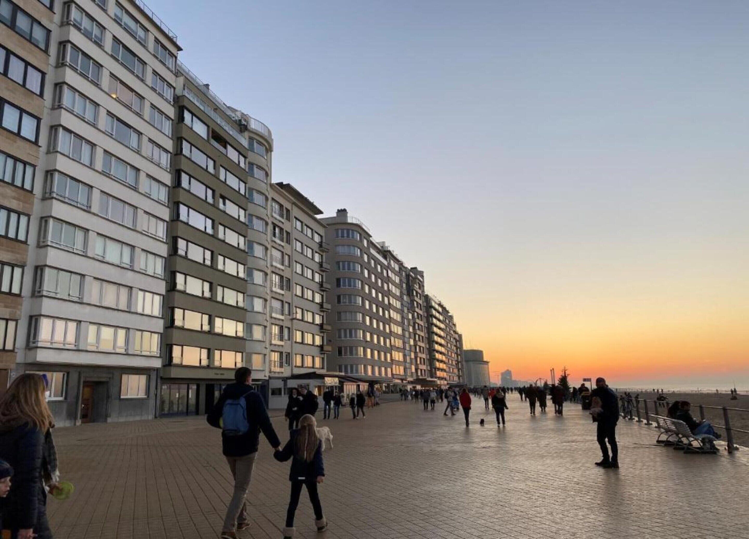 A promenade with modern buildings, a clear sky, and people walking.