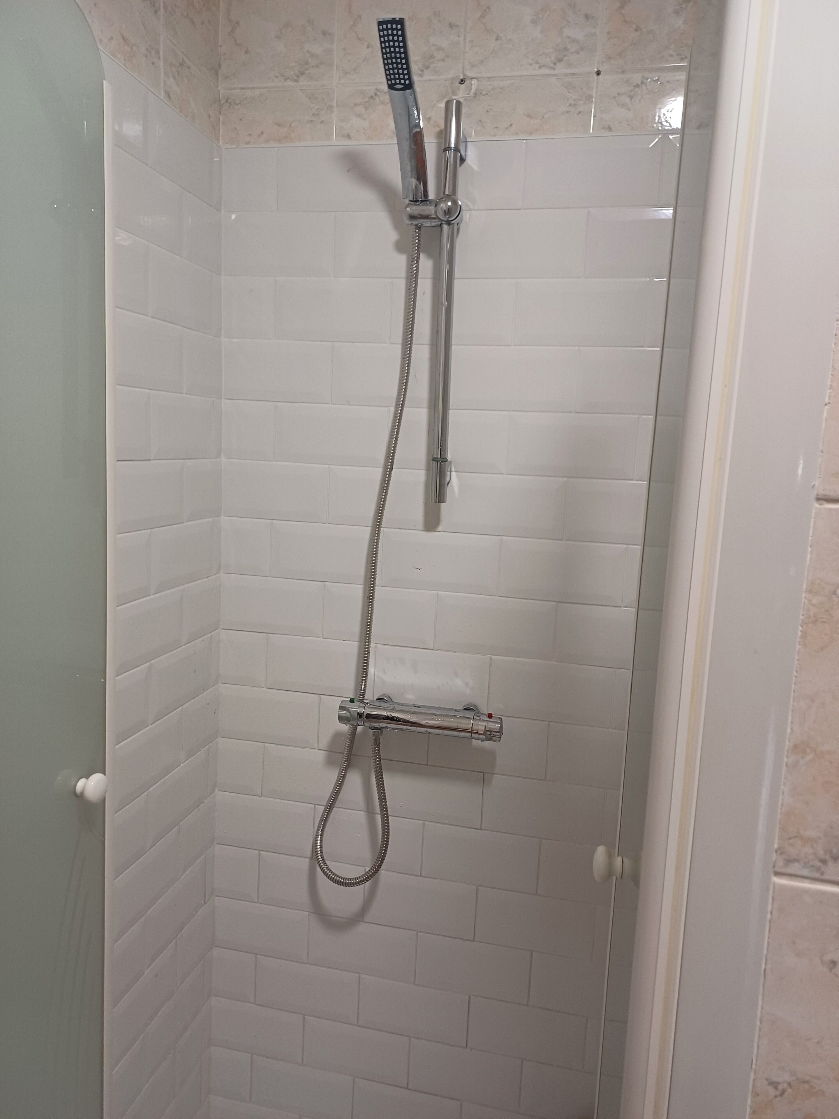 Une douche équipée d’un pommeau de douche à main et d’un pommeau de douche fixe, tous deux fixés sur un mur recouvert de carreaux blancs.