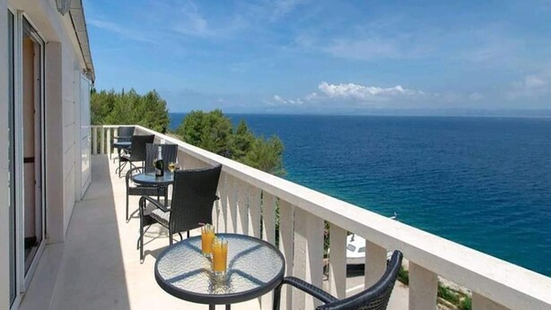 A balcony with a table and chairs overlooking the sea.