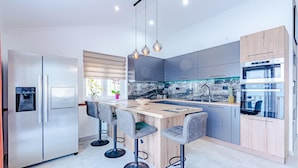 A modern kitchen with a central island, bar stools, stainless steel appliances, and a marble backsplash.