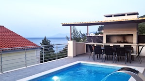 A rooftop pool with a barbecue area and dining setup overlooking the sea.