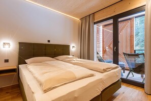 A bedroom with two beds, a wooden ceiling, a sliding glass door leading to an outdoor area with a chair. - Premium Suite in Saalbach (Saalbach-Hinterglemm)