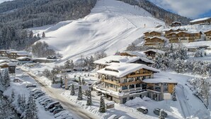 Une station de ski enneigée, avec plusieurs bâtiments, dont un grand chalet d’où l’on aperçoit un télésiège au loin.