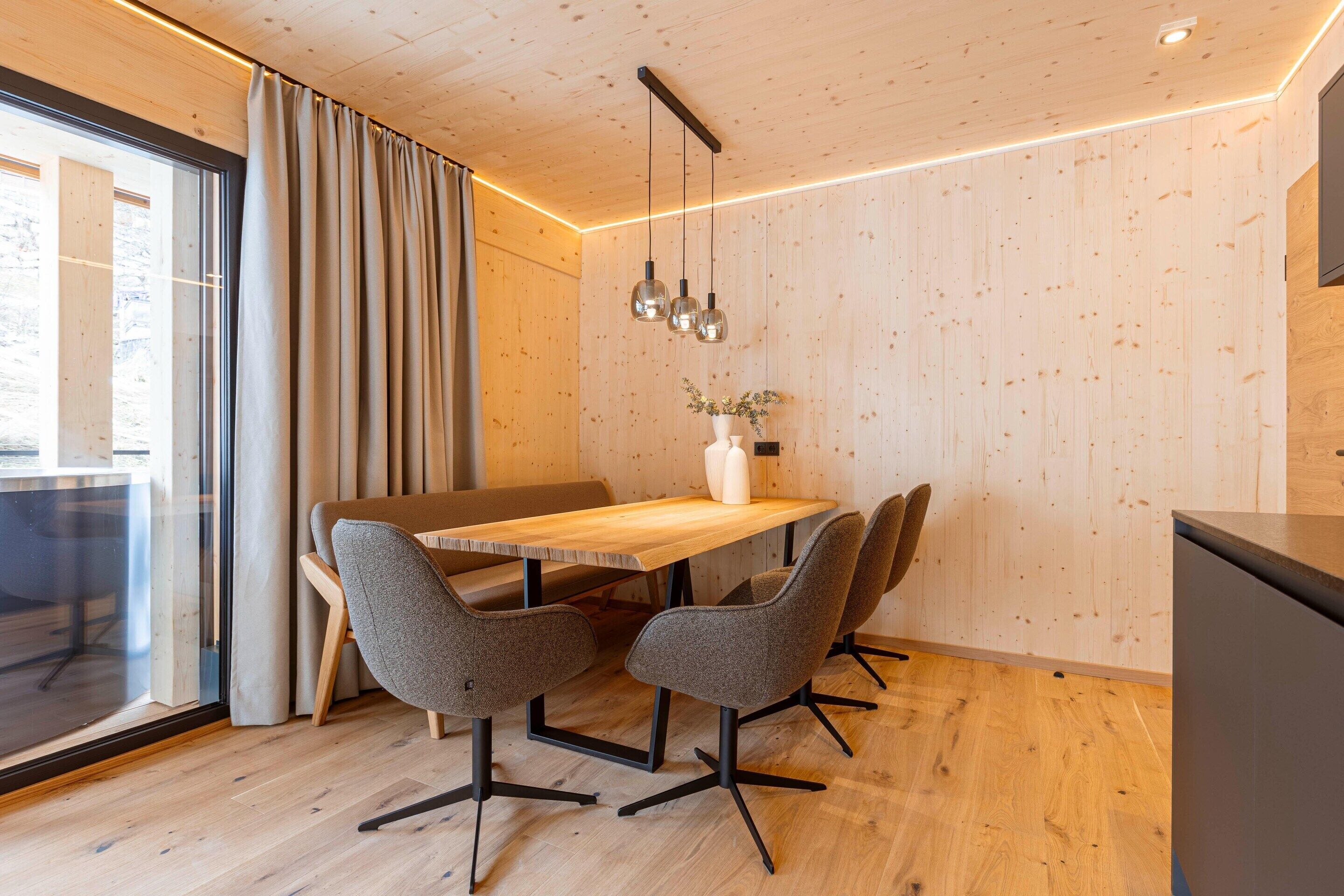 Een moderne eetruimte met een houten tafel, vier grijze stoelen, een vaas met bloemen en hanglampen.