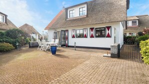 Een huis met rieten dak, witte muren en een terras van bakstenen.