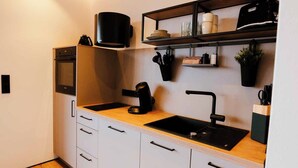 A compact kitchen with a built-in oven, a coffee machine, a sink, and a shelf with kitchen utensils. - SeeZeit at Walchsee (Walchsee)