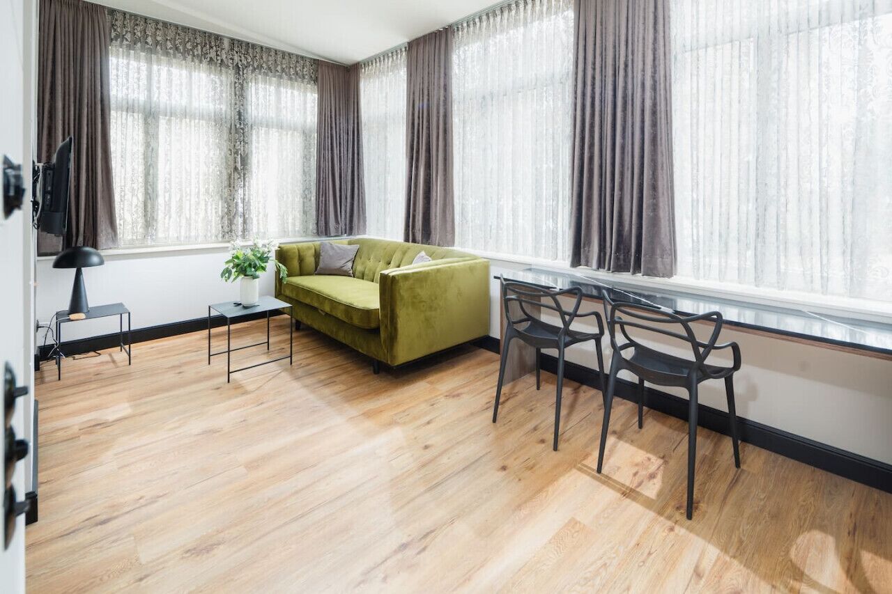 A living room with a green sofa, two black chairs, a small table, and a plant.